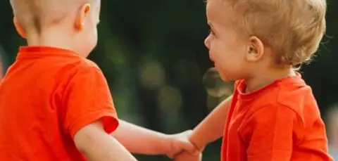 Dos infants amb samarreta taronja agafats de la mà